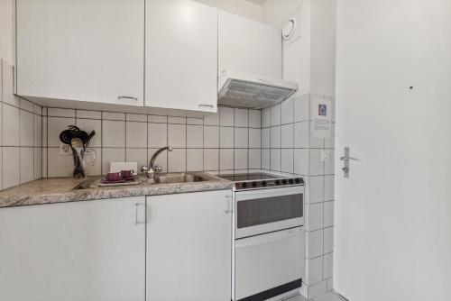 a white kitchen with white cabinets and a sink at Athénée 36 Résidence by Homenhancement in Geneva