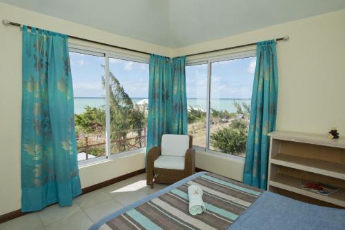 a bedroom with a bed and a chair and windows at Le Refuge in Rodrigues Island