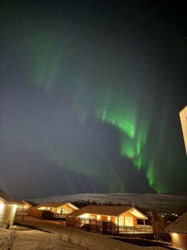an aurora lights up the sky over buildings at Hotel Kjarnalundur- Aurora Dream - Lodges and Rooms in Akureyri