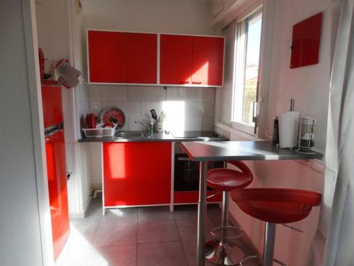 une cuisine rouge avec des placards et des tabourets rouges dans l'établissement Parking privé,T1 bis, 10mn Lyon centre, à Villeurbanne
