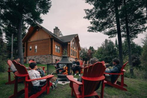 a group of people sitting around a fire in front of a log cabin at Chalet Red Deer Spa at Fiddler Lake in Mille-Isles