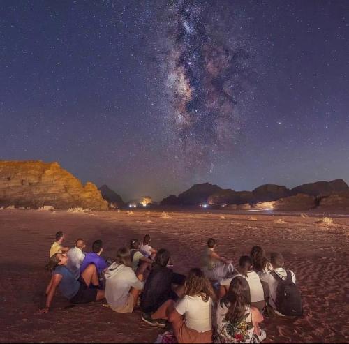 a group of people sitting on the beach at night at WADI RUM WINGS lUXURY CAMP in Wadi Rum