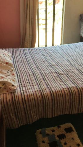 a bed with a striped comforter and a window at Habitación en Casa Familiar 