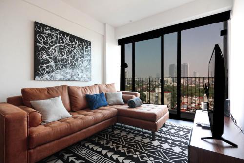 a living room with a brown leather couch and large windows at Lujoso y cómodo departamento en la mejor zona de Condesa in Mexico City