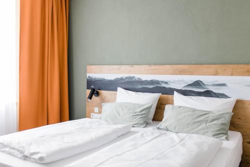 a bed with two white pillows and an orange curtain at Stadthotel Freilassing in Freilassing