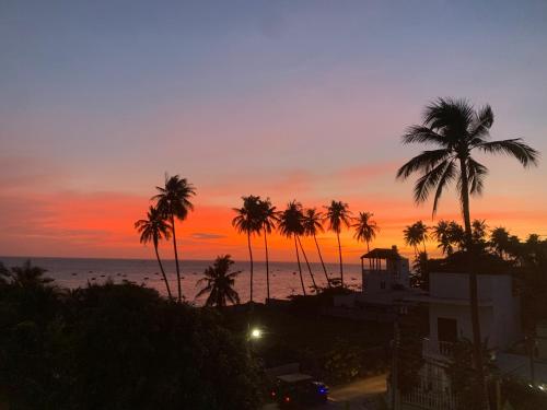 a sunset with palm trees in front of the ocean at A L Y S S A Seaside Muine in Mui Ne