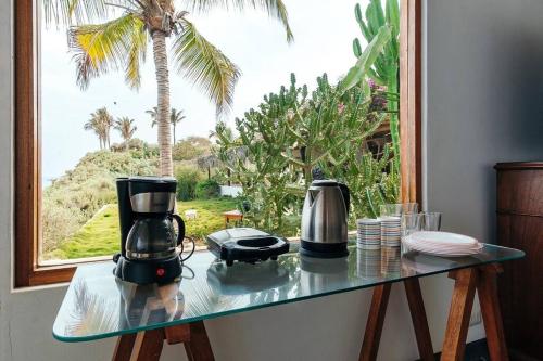 a glass table with two coffee makers on it in front of a window at Marmot Seashore Moonset Suite in Máncora