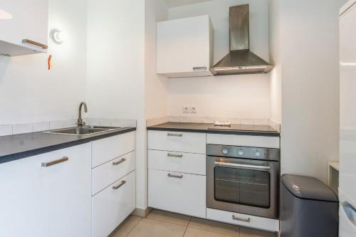 une cuisine avec des armoires blanches, un évier et une cuisinière dans l'établissement Appartement Juanesco - Welkeys, à Juan-les-Pins