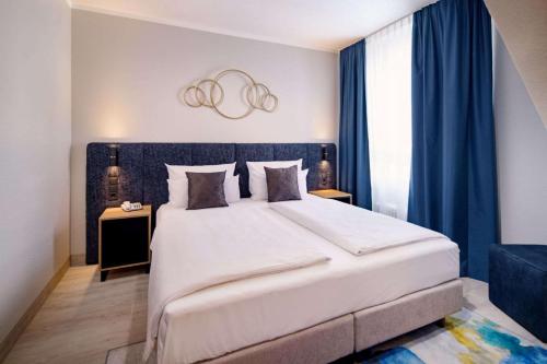 1 dormitorio con 1 cama blanca grande y cortinas azules en Aspire Elements Reutlingen, Trademark Collection by Wyndham, en Reutlingen