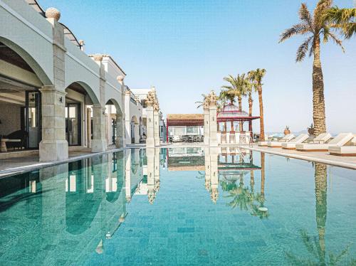 una piscina con palmeras y un edificio en Grecotel Plaza Beach House, en Rethymno