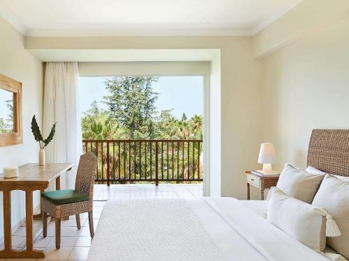 a bedroom with a bed and a desk and a balcony at Grecotel Filoxenia Hotel in Kalamata