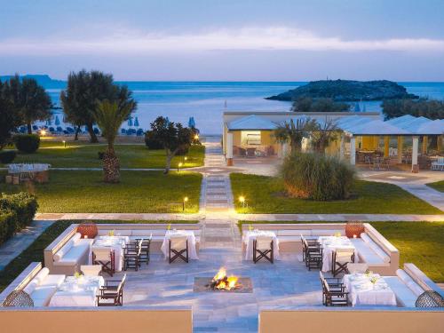 an outdoor dining area with tables and chairs and the ocean at Grecotel Meli Palace in Sisi