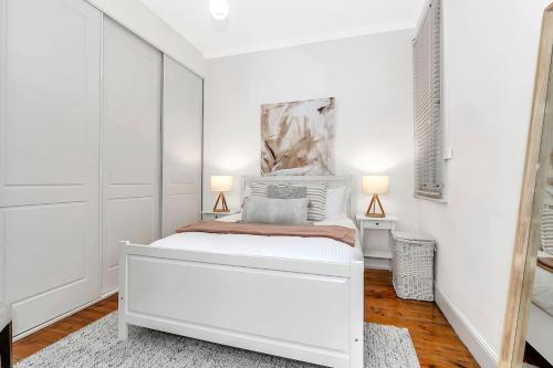 a white bedroom with a bed and two lamps at 'Violet Cottage' An Idyllic Urban Oasis for Two in Unley