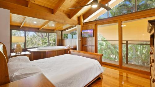 a bedroom with a bed and a tub and windows at Rainforest Treehouse Sanctuary - with ocean views in Smithfield