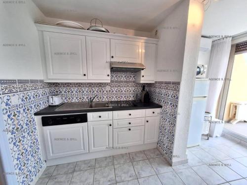 - une cuisine avec des placards blancs et du carrelage bleu et blanc dans l'établissement Résidence Héliopolis Bâtiment C - Héliopolis Bât. C studio 2 Pers. MAE-1871, au Cap d'Agde