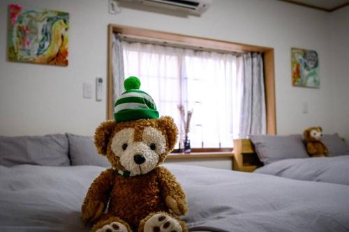 a teddy bear wearing a green hat sitting on a bed at 难波站 高岛屋步行5分钟 双层独栋别墅150平 4卧室3厕所2浴室 空间宽敞设施齐全 八阪神社步行1分钟 心斋桥 道顿堀 黑门市场 通天阁步行圈内 in Osaka