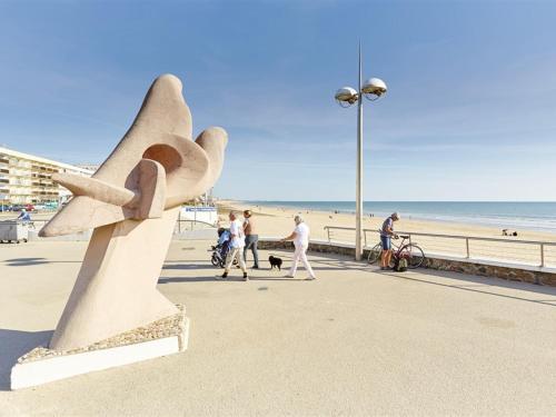 une sculpture sur la plage avec des personnes marchant avec un chien dans l'établissement Studio face à la mer avec balcon et parking - 4 pers, Saint-Jean-de-Monts - FR-1-323-428, à Saint-Jean-de-Monts