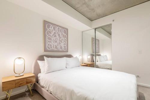 een witte slaapkamer met een bed en een spiegel bij Urban Hideaway in Melbourne's Epicentre in Melbourne