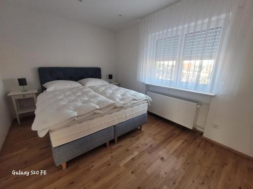 a white bedroom with a bed and two windows at Modernes Ferienappartement An der Steige in Wilhermsdorf