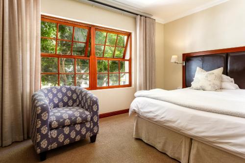 a bedroom with a bed and a chair and a window at Noordhoek Village Hotel in Noordhoek