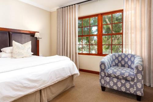 a bedroom with a bed and a chair and a window at Noordhoek Village Hotel in Noordhoek