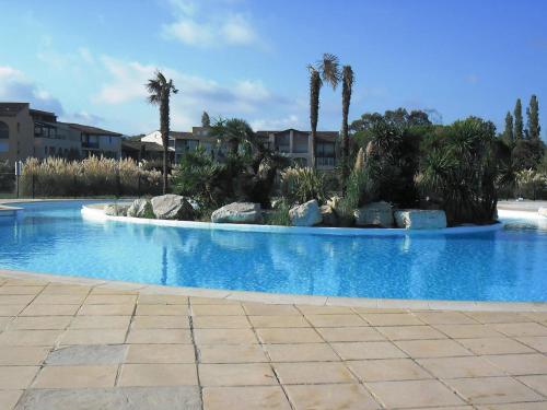 een groot blauw zwembad met palmbomen en rotsen bij GASBRU - Golfe de St-Tropez - Rez de jardin T2 cabine avec accès plage piscine et tennis in Gassin