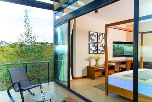 1 dormitorio con balcón, cama y escritorio en Glass House at Champagne Ridge Villa by YourHost, en Nairobi
