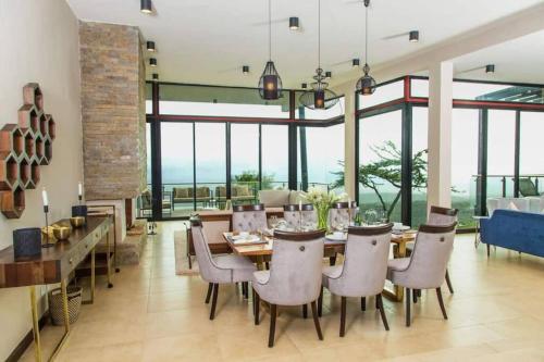 comedor con mesa, sillas y ventanas en Glass House at Champagne Ridge Villa by YourHost, en Nairobi