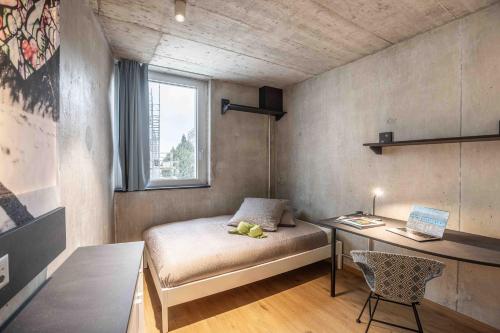 a bedroom with a bed and a desk and a window at Lumen by coliving in Renens