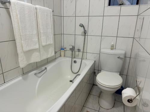 a white bathroom with a toilet and a bath tub at Busa House in White River