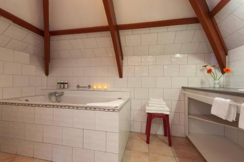 a white tiled bathroom with a tub and a stool at Hotel Pension 't Huys Grol in Renesse
