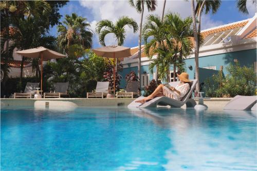 a woman sitting in a chair next to a swimming pool at Kura Botanica Hotel in Willemstad