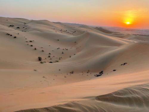 a sunset in the desert with a sand dune at Liwa Hotel in Mezairaa