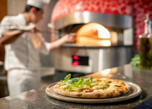 a pizza on a counter with a person in a kitchen at Elexus Hotel Resort & Spa & Casino in Kérynia