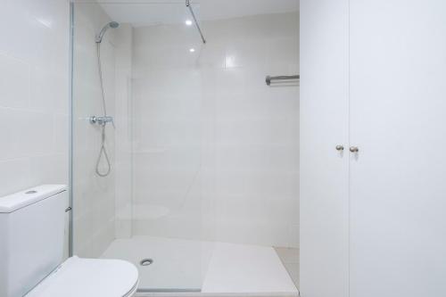 uma casa de banho branca com um chuveiro e um WC. em Centric Apartment Camp Nou em Hospitalet de Llobregat