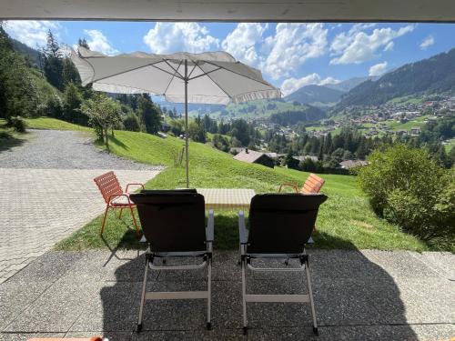 duas cadeiras e uma mesa com um guarda-sol em Apartment Shalom by Interhome em Adelboden