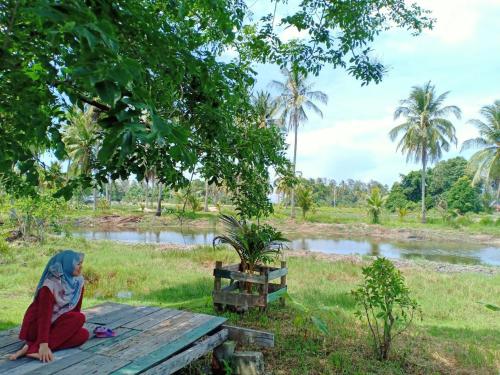 a woman sitting on a picnic table in front of a river at Homestay Umar Homestay Tilam Hotel in Bachok
