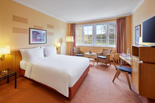 ein Hotelzimmer mit einem großen weißen Bett und einem Schreibtisch in der Unterkunft Lindner Hotel Wiesensee in Westerburg