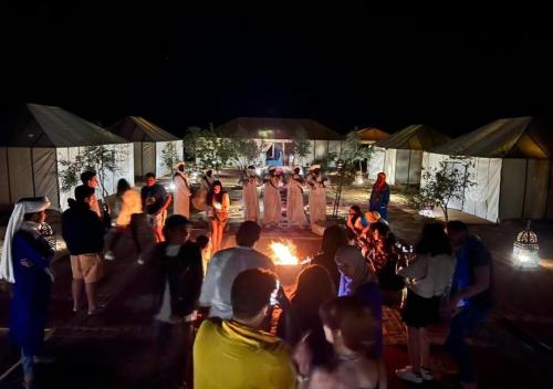 a group of people standing around a fire at night at Desert Luxury Tented & Activities in Hassilabied