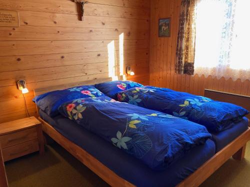 a bed in a wooden room with blue sheets at Chalet Bambi in Rosswald