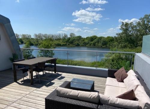 a patio with a couch and a table and a view of a river at Reed Warbler - HM111 - Lower Mill Estate Penthouse Apartment with Spa Access in Somerford Keynes