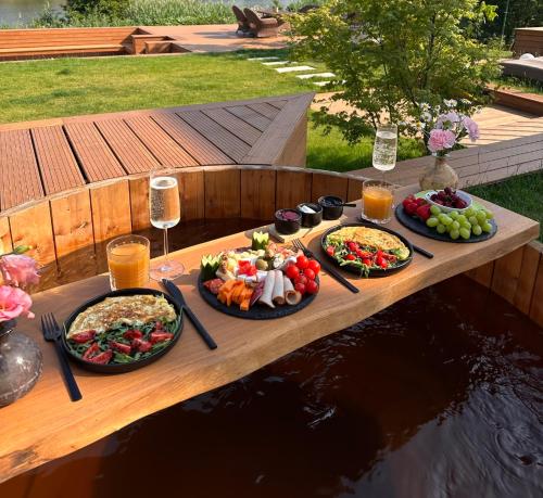 a wooden table with plates of food and drinks at A-BY THE LAKE - PRIVATE A FRAME VILLAS in Căciulaţi