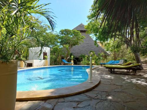 een zwembad in een tuin met stoelen en bomen bij Watamu Beach Cottages B&B in Watamu