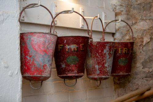 a group of red buckets hanging on a wall at The Fireman's House, Lowe's Mill Cottages at Torr Vale Mill in New Mills