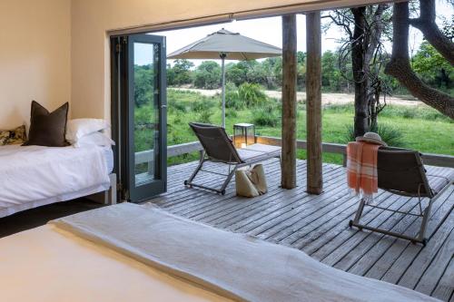 a bedroom with a bed and chairs on a wooden deck at Simbavati River Lodge in Timbavati Game Reserve
