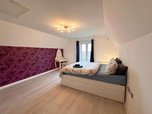 a bedroom with a bed and a purple accent wall at 4 Bed Town House with free parking in Eaton Socon