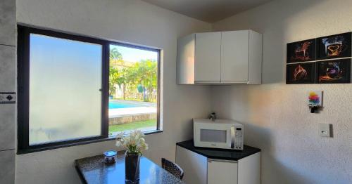 a kitchen with a table with a microwave and a window at Apart Hotel Farol de Itapuã - Duas suítes com cozinha completa à 250m da praia e farol de Itapuã in Salvador