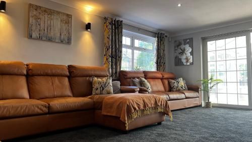 a brown leather couch in a room with windows at The Cheshire Gathering - Sleeps up to 30 With Hot Tub in Chester