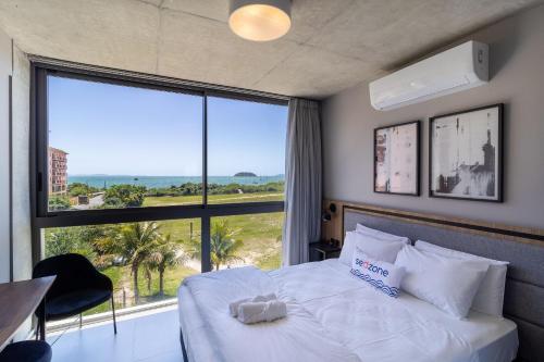 1 dormitorio con cama blanca y ventana grande en Spot Jurere sofisticação à beira mar - SPJ's, en Florianópolis