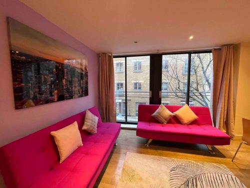 a living room with a pink couch and large windows at Bright Flat in Bricklane-Aldgate in London